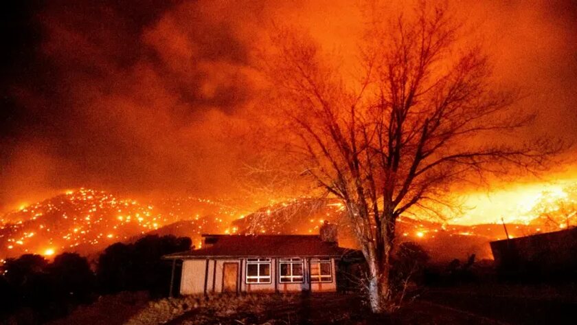 Wildfire burning across dark hillsides at night behind a small single-storey house
