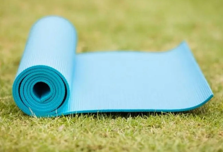 A rolled-up blue exercise mat lying on grass